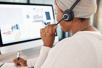 Closeup of one african american call centre telemarketing agent from behind talking on a headset while working on a computer in an office. Hands and face of female consultant operating a helpdesk for customer service and sales support