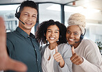 Portrait of a diverse group of happy smiling call centre telemarketing agents gesturing thumbs up while taking selfies together in an office. Confident and ambitious colleagues determined to provide the best customer service and sales support
