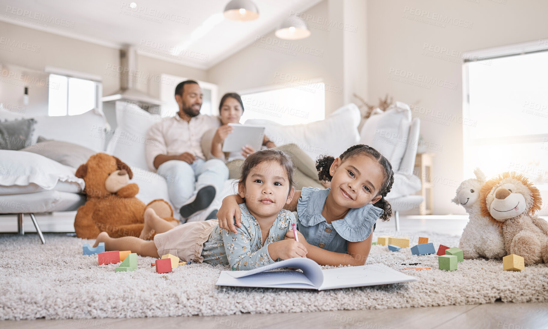 Buy stock photo Little two girls drawing with colouring pencils lying on living room floor with their parents relaxing on couch. Little children sisters siblings colouring in during family time at home