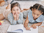 Little two girls drawing with colouring pencils lying on living room floor with their parents relaxing on couch. Little children sisters siblings colouring in during family time at home