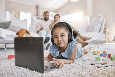 Buy stock photo Closeup of a little cute girl using a laptop and wireless headphones while laying on the floor in the lounge. Hispanic girl using a wireless device to do her homework in the living room