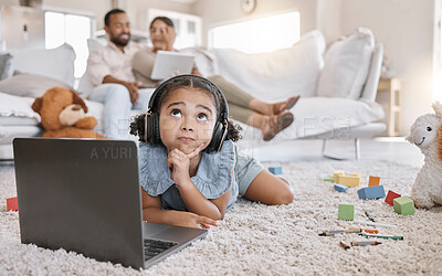 Buy stock photo Closeup of a little cute girl using a laptop and wireless headphones while laying on the floor in the lounge. Hispanic girl using a wireless device to do her homework in the living room