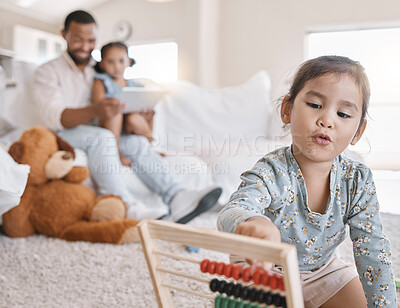 Buy stock photo Closeup of a little girl using a abacus while sitting on the floor in the lounge while her father and sister using a digital tablet on the sofa at home