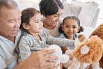 Closeup of to mixed race grandparents playing with their granddaughters and their teddy bears on the sofa at home. Family having a fun time at home
