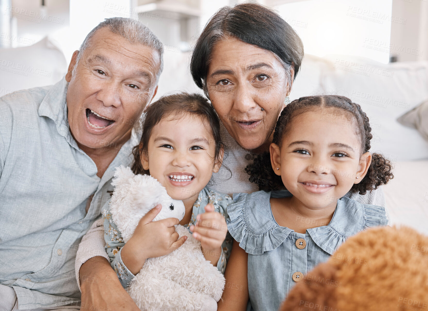 Buy stock photo Closeup of to mixed race grandparents playing with their granddaughters and their teddy bears on the sofa at home. Family having a fun time at home