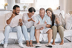 Mixed race family celebrating while watching sport on a tablet and sitting on the sofa in the lounge at home. Hispanic family looking ecstatic while using a wireless device in the living room