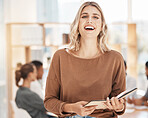 Portrait of a confident young caucasian businesswoman laughing while holding notebook planner in an office with her colleagues in the background. Cheerful ambitious entrepreneur and determined leader ready for success in a startup with her team