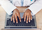Above closeup african american woman doctor using a laptop computer while working at a desk in her hospital office. Using wireless technology to diagnose diseases in the field of health and medicine