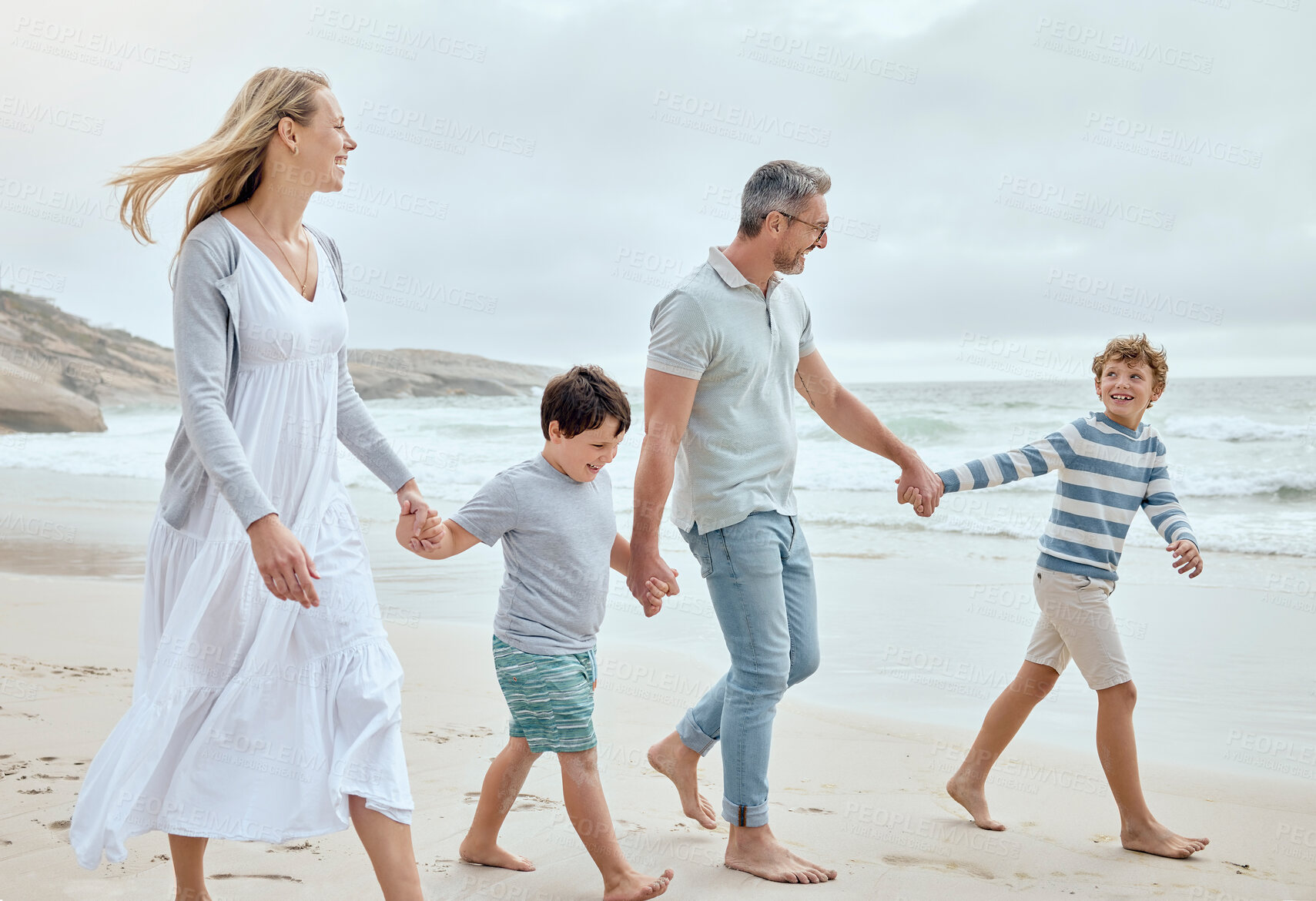 Buy stock photo Happy caucasian parents and kids holding hands while walking together along the beach shore during a relaxing fun family summer vacation. Loving mom and dad enjoying leisurely stroll while bonding with little sons