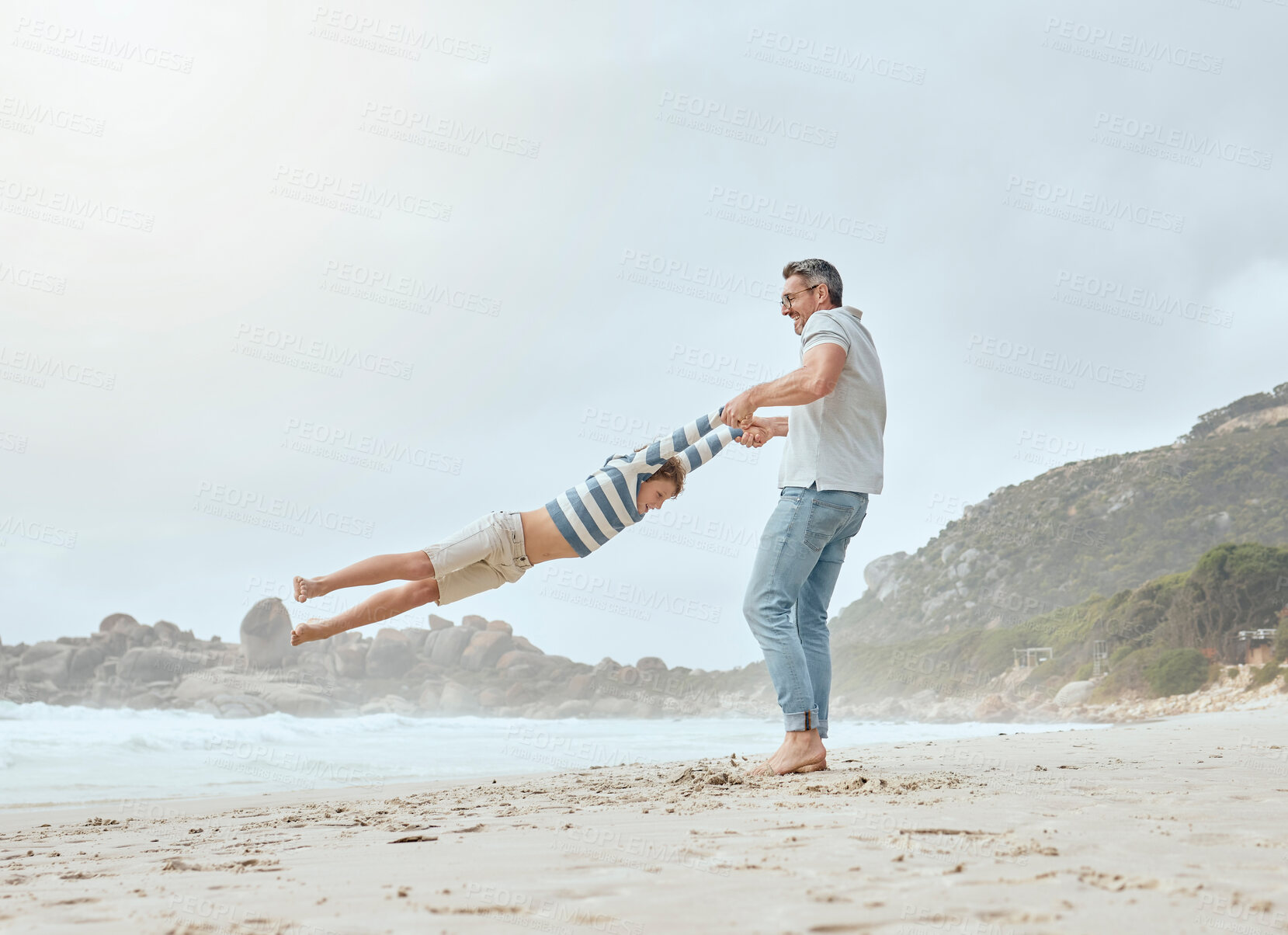 Buy stock photo Happy caucasian father swinging and spinning his cute son in circles by the arms at the beach. Playful kid having fun while bonding with dad on sunny summer vacation outdoors