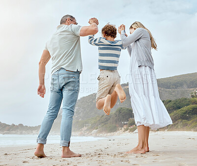 Buy stock photo Happy caucasian parents from the back holding hands with their cute little playful son and swinging him up at the beach. Cheerful kid jumping and having fun while bonding with mom and dad on family summer vacation together