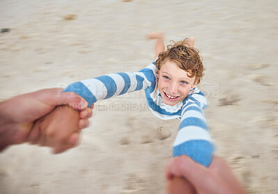 Happy caucasian boy swinging and spinning in circles by the arms at the beach shore with his father. Face of cute playful kid having fun while bonding with a parent on sunny summer vacation outdoors
