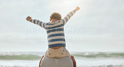 Cute little caucasian boy from behind cheering with arms outstretched while sitting on his father\'s shoulders at the beach. Playful young child from the back having fun and bonding with dad outdoors. The innocence of childhood