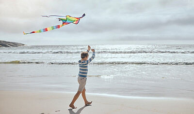 Buy stock photo One little caucasian boy flying a colourful rainbow kite in the wind at the beach. Playful young child having fun outdoors. The innocence of childhood