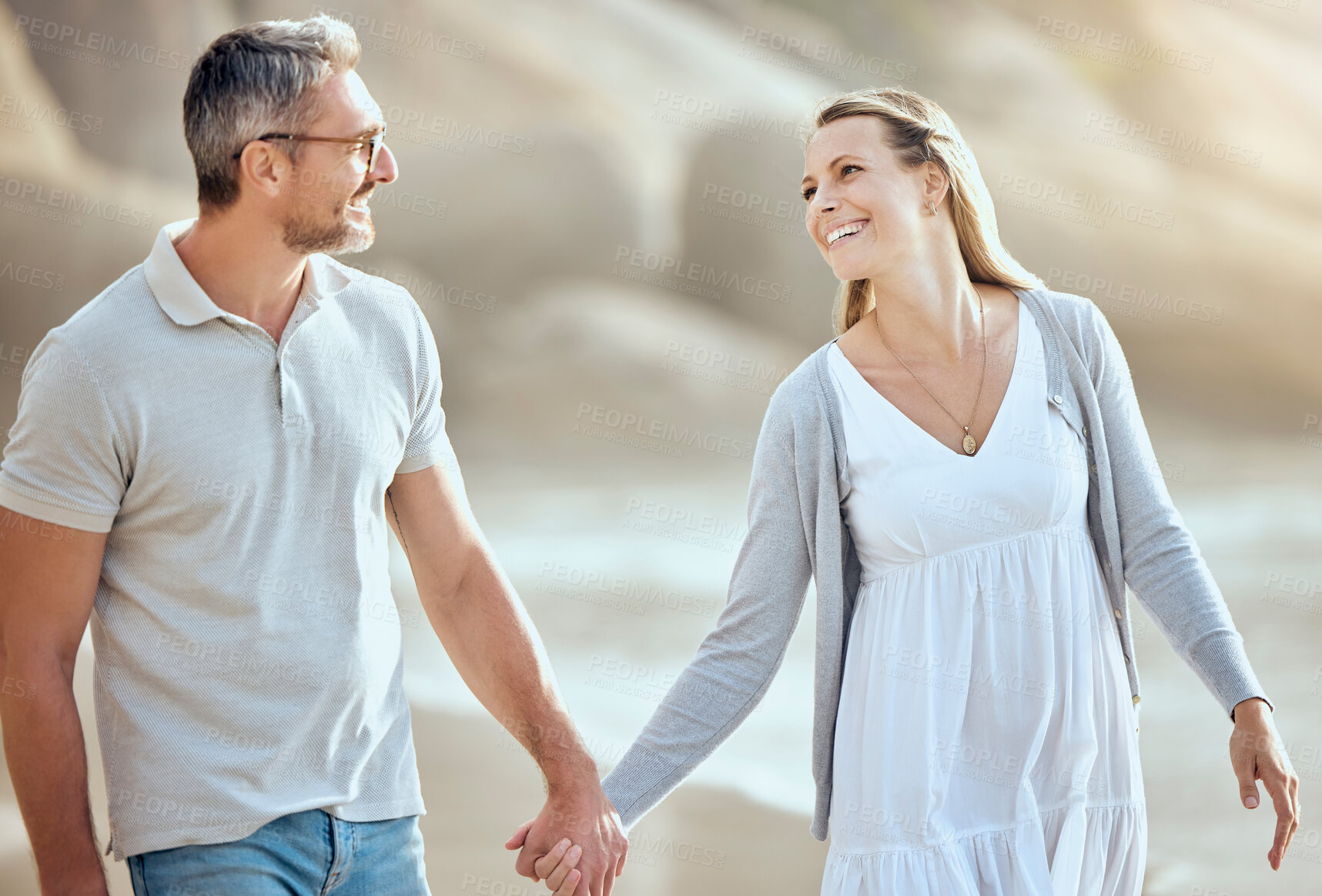 Buy stock photo Happy and loving mature caucasian couple enjoying a romantic walk at the beach together on a sunny day. Cheerful affectionate husband and wife holding hands while bonding on vacation outdoors