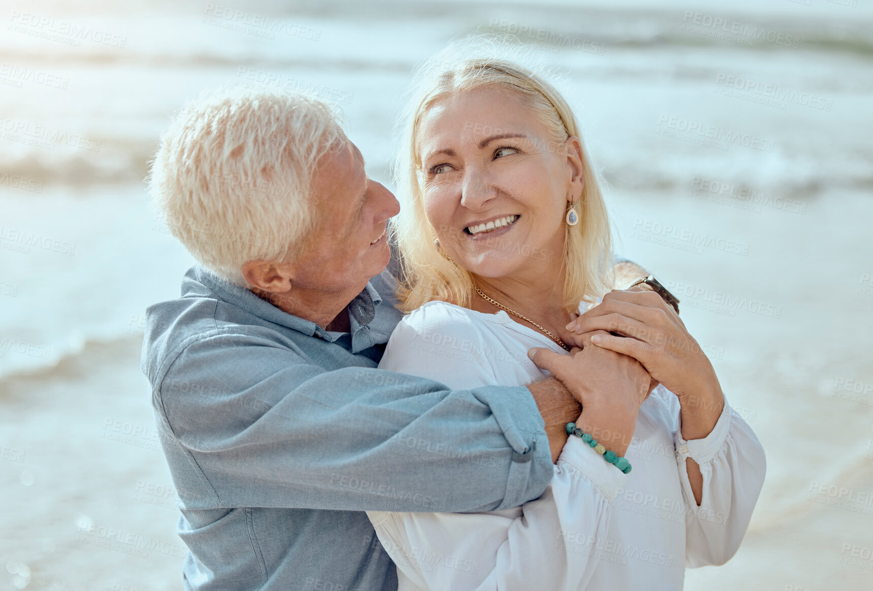 Buy stock photo A happy mature caucasian couple enjoying fresh air on vacation at the beach. Smiling retired couple hugging and embracing while bonding outside together