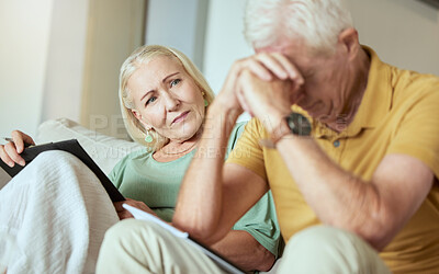 Unhappy elderly couple sitting on a sofa together and looking stressed. Senior caucasian man and woman looking worried about their future while looking at paperwork and their debt