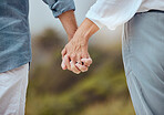 Closeup of a mature couple holding hands and enjoying a romantic stroll together on vacation at the beach. Older couple holding hands outside