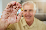 An happy man showing his pills while sitting at home. Smiling mature man taking his daily treatment for chronic disease and illness