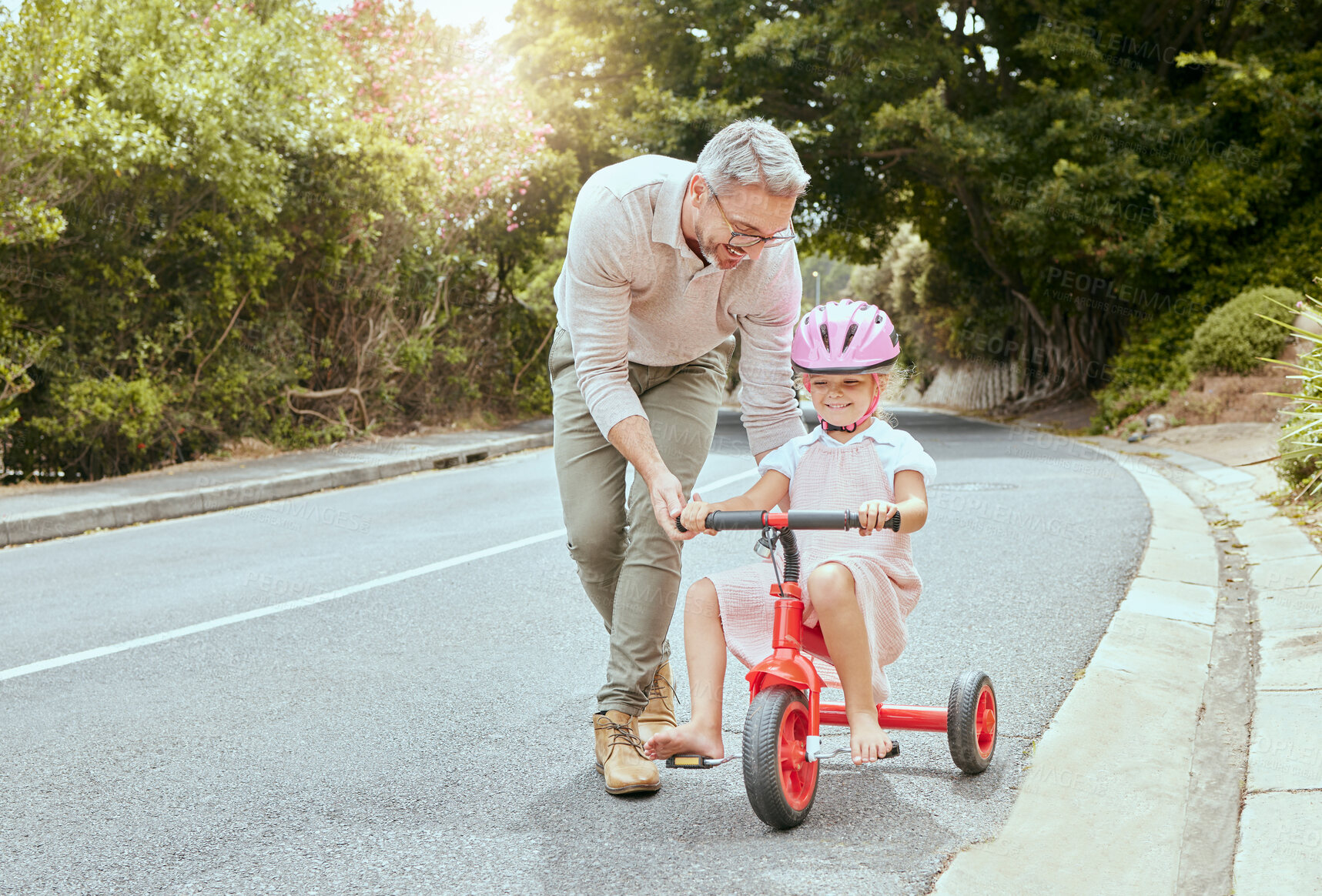 Buy stock photo A happy father teaching his little girl to ride a bike outside. Cute Caucasian child wearing a pink helmet and cycling while bonding with her dad