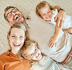 A happy Caucasian family of four lying in the living room at home. Loving smiling family being affectionate on the lounge floor. Young couple bonding with their  little kids at home