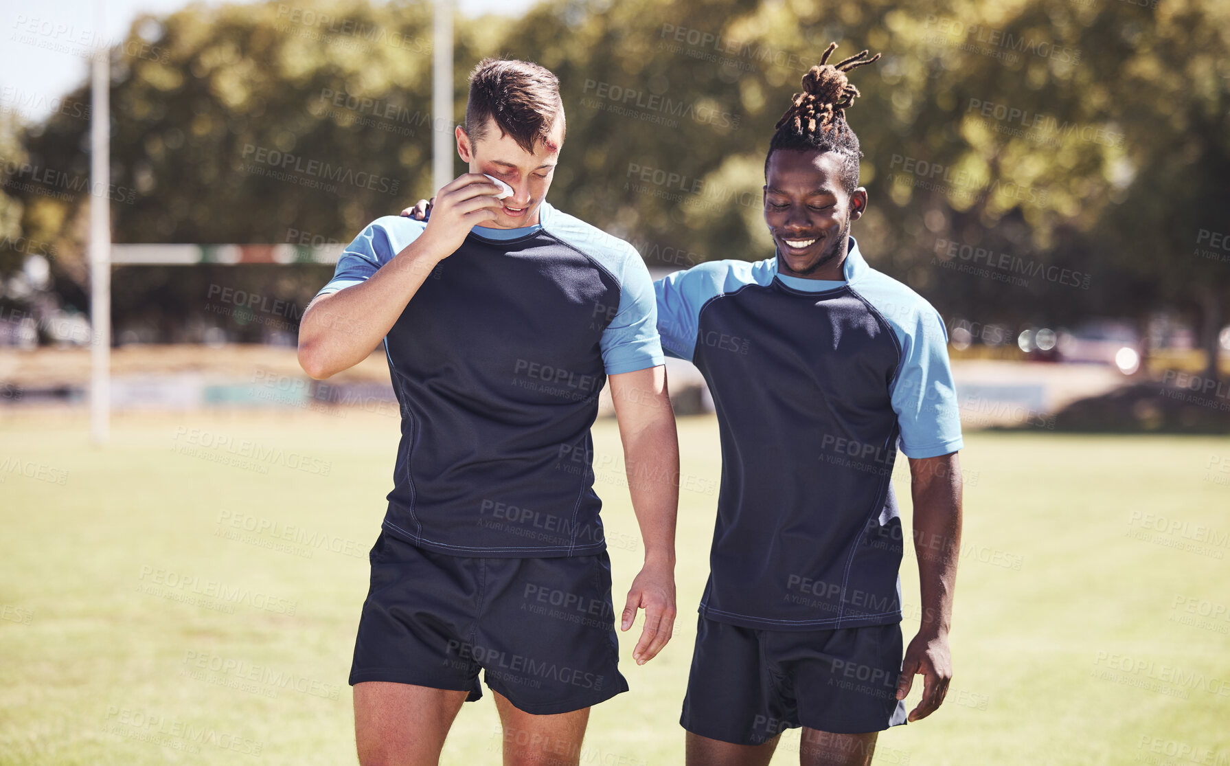 Buy stock photo Two diverse young rugby players standing outside on the field. Black man smiling while talking to his injured and bruised caucasian teammate. Athletic sportsmen discussing and reflecting on the game