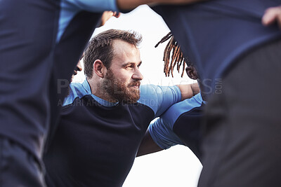 Buy stock photo Below caucasian rugby player standing in a huddle with his teammates outside on a field. Young male athlete looking serious and focused while huddled together with his team. Ready for the game