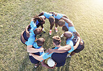 Above diverse group of rugby players standing in a huddle together outside on a field. Young male athletes looking serious and focused while huddled together as a team. Ready for a tough game