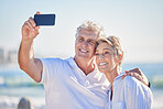 A happy mature caucasian couple enjoying fresh air on vacation at the beach while using a cellphone. Smiling retired couple hugging and taking selfies together outside