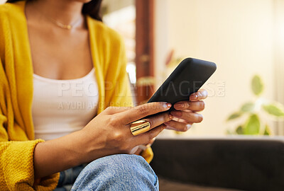 Closeup of woman using her smartphone while sitting on a sofa in a bright living room. A young hispanic female texting on her cellphone using modern technology at home
