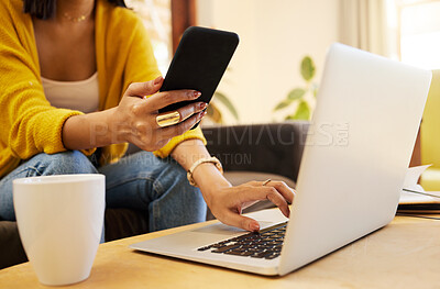 Buy stock photo Closeup of woman working remote while typing on her laptop and holding her smartphone sitting on a sofa in a bright living room. One focused hispanic young female at home using modern technology