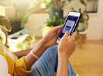 Closeup of a woman banking online while holding her smartphone sitting in a bright living room. A hispanic young female at home using modern technology to pay investments.