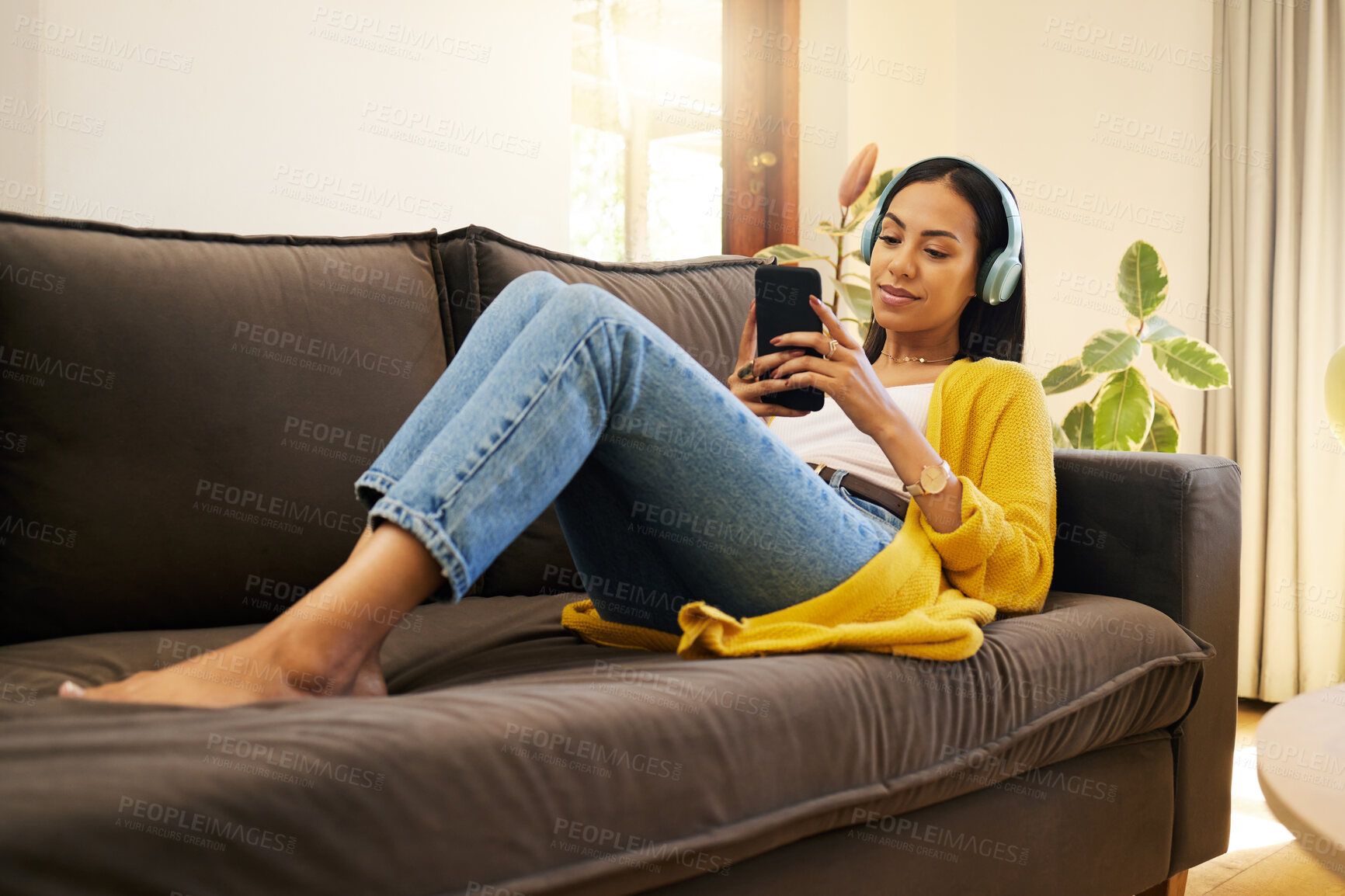 Buy stock photo Woman, relax and phone on social media or entertainment streaming online at home on the living room sofa. Young female relaxing on a couch listening to music with headphones on mobile smartphone