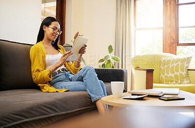 Woman using her tablet while relaxing in a bright living room. A young female with glasses sitting on a sofa scrolling on her digital tablet at home using modern technology during lockdown