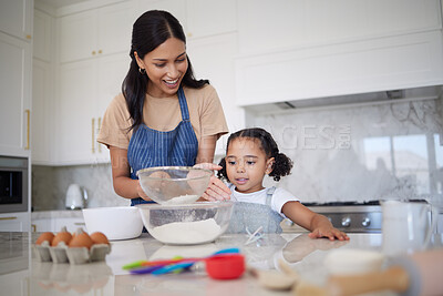 Caring single mother and small adorable daughter baking together in a kitchen at home. Smiling mother teaching cute little girl how to sieve flour. Happy single parent and curious child bonding inside