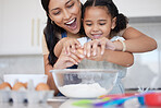 Happy young mixed race mother enjoying baking with her little daughter and cracking a egg in the kitchen at home. Little hispanic girl smiling while helping her mother cook a meal at home. Child cracking egg for recipe