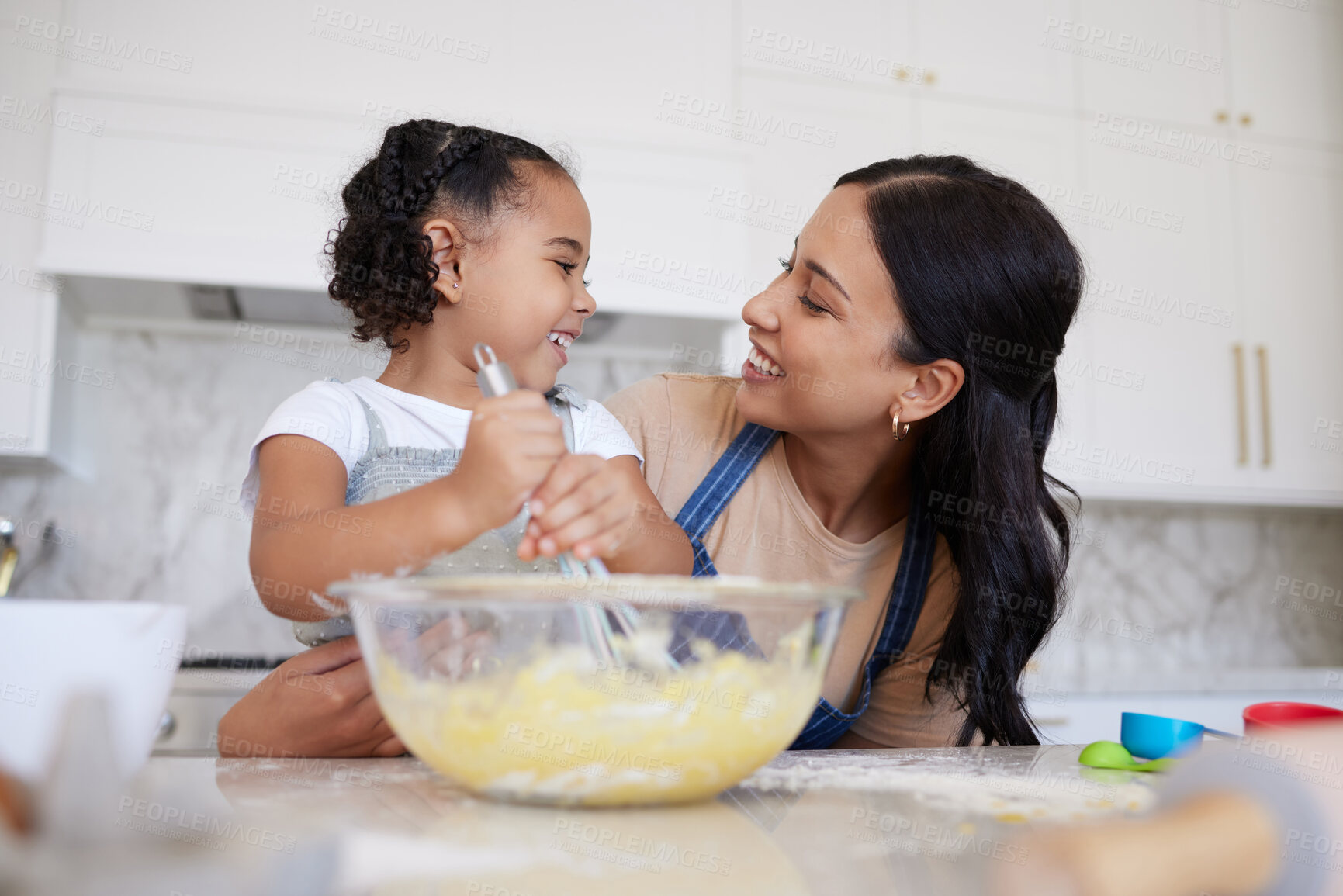 Buy stock photo Happy mixed race mother and daughter baking and bonding. Young woman helping her daughter bake at home. Smiling mother holding an egg, cooking with her daughter. Happy little mixing a bowl of batter