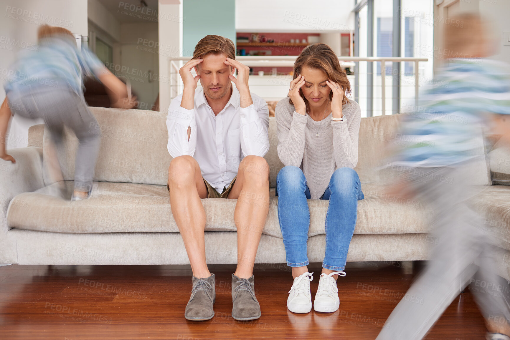 Buy stock photo Naughty hyperactive, energetic children annoying their mother and father at home. Tired and stressed parents suffering from a headache and fatigue while adhd kids run around living room being noisy. 