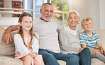 A happy caucasian mature couple bonding with their adopted kids in the living room. Two siblings relaxing with their grandparents together at home on a couch. Sister and brother visiting grandparents
