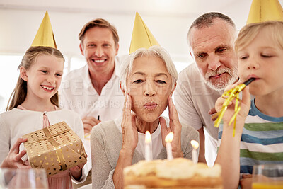 Buy stock photo Senior woman celebrating a birthday with family at home, wearing party hats and blowing whistles. Grandma looking at birthday cake and being joyful while surrounded by her grandkids, husband and son