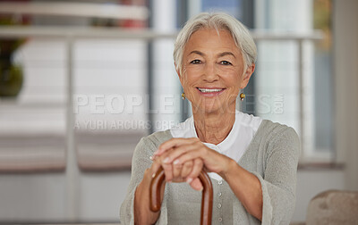 Buy stock photo Portrait of a retired senior woman holding a wooden cane and smiling while sitting at home. Happy old lady leaning on a walking stick for support and enjoying her stay at a retirement facility