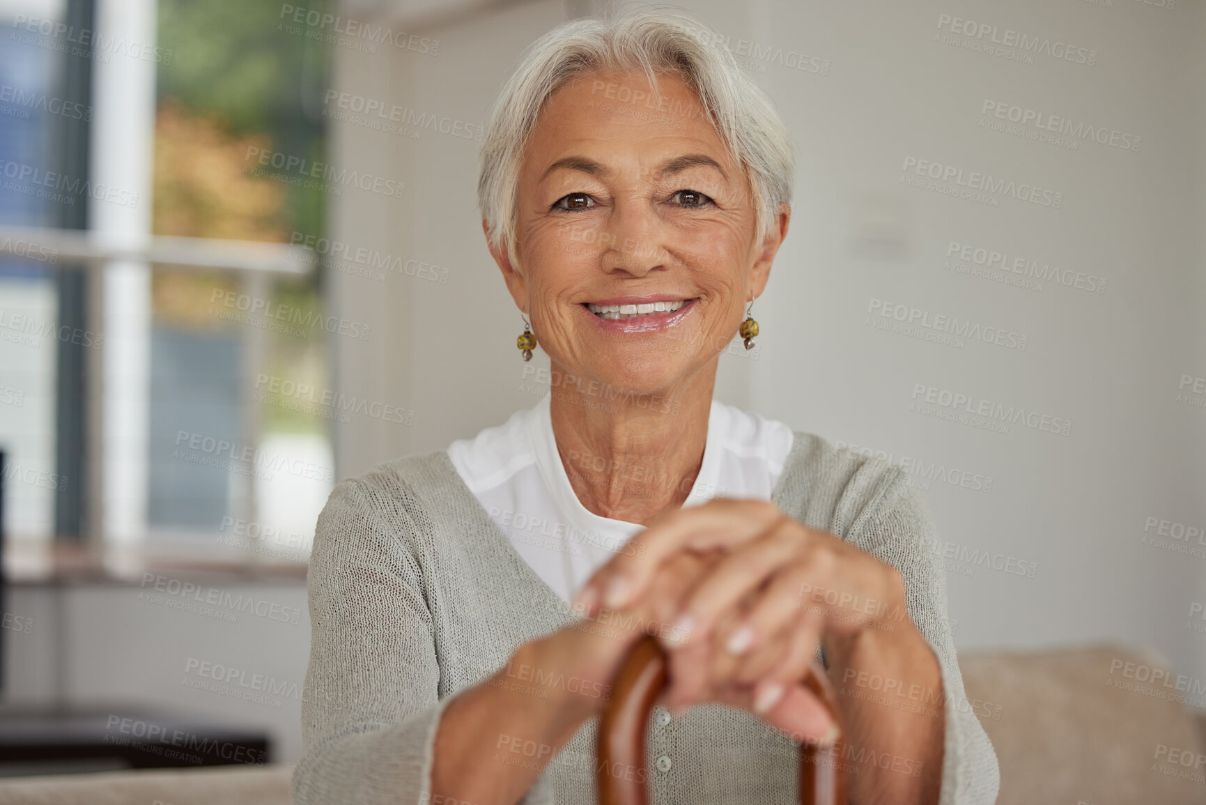 Buy stock photo Retired senior woman relaxing at home. Happy smiling old woman holding walking cane and looking at the camera with positivity. Carefree and mature grandmother sitting on chair in nursing home