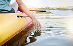 Close up of female hands feeling lake water while kayaking during the day. Active young woman enjoying water activity while on vacation. Canoeing on sunset lake