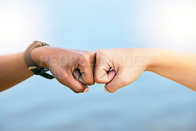 Closeup of two unknown people giving each other a fist bump against blue copyspace. Female friends feeling supported, united and touching fists at the knuckles. Feeling motivated and ready to achieve