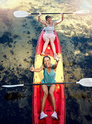 Above portrait two diverse young woman cheering and celebrating while canoeing on a lake. Excited friends enjoying rowing and kayaking on a river while on holiday or vacation. A weekend getaway
