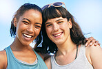 Portrait of two smiling friends embracing while standing together against blue sky. Smiling happy young women bonding and hugging outside over summer break. Close best friends having fun on a weekend