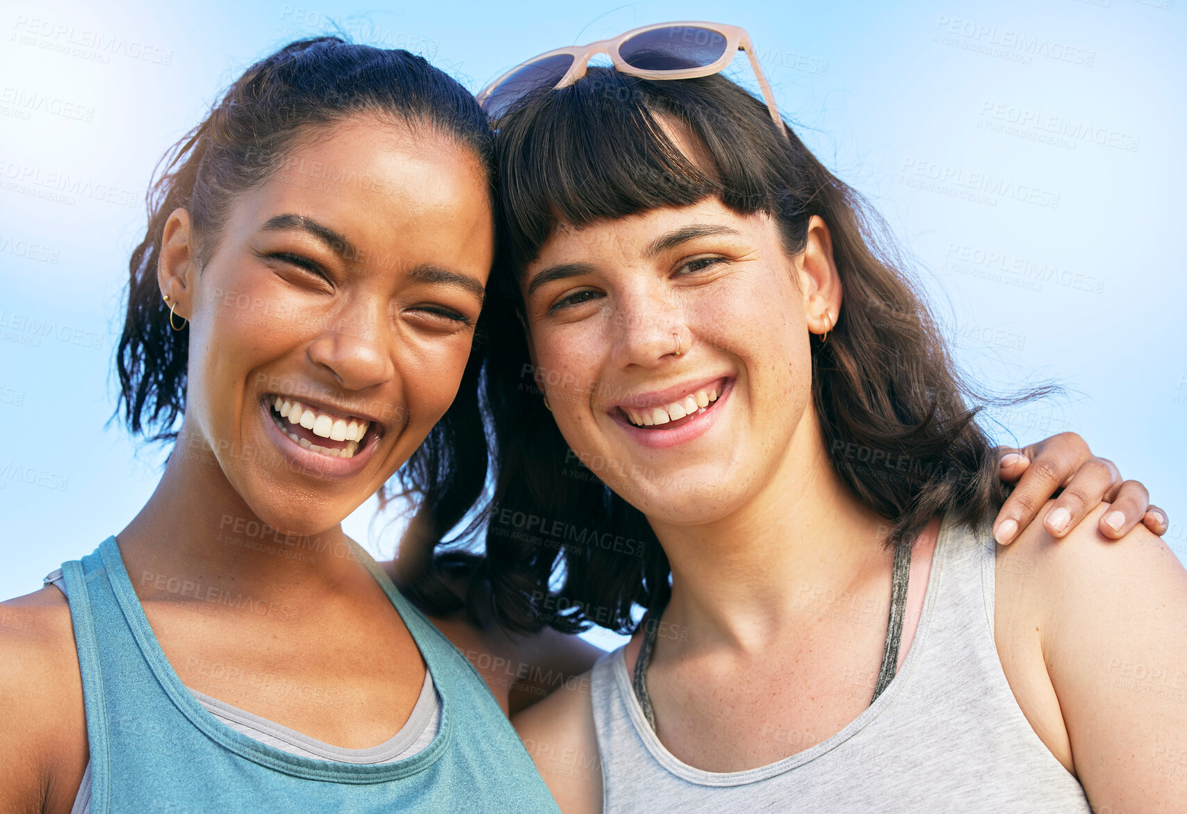Buy stock photo Portrait of two smiling friends embracing while standing together against blue sky. Smiling happy young women bonding and hugging outside over summer break. Close best friends having fun on a weekend