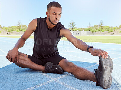 Buy stock photo Male runner doing stretching exercises while sitting on sports track. Determined young male athlete sitting alone and warming up his muscles before going for a run. Fitness man preparing for a race