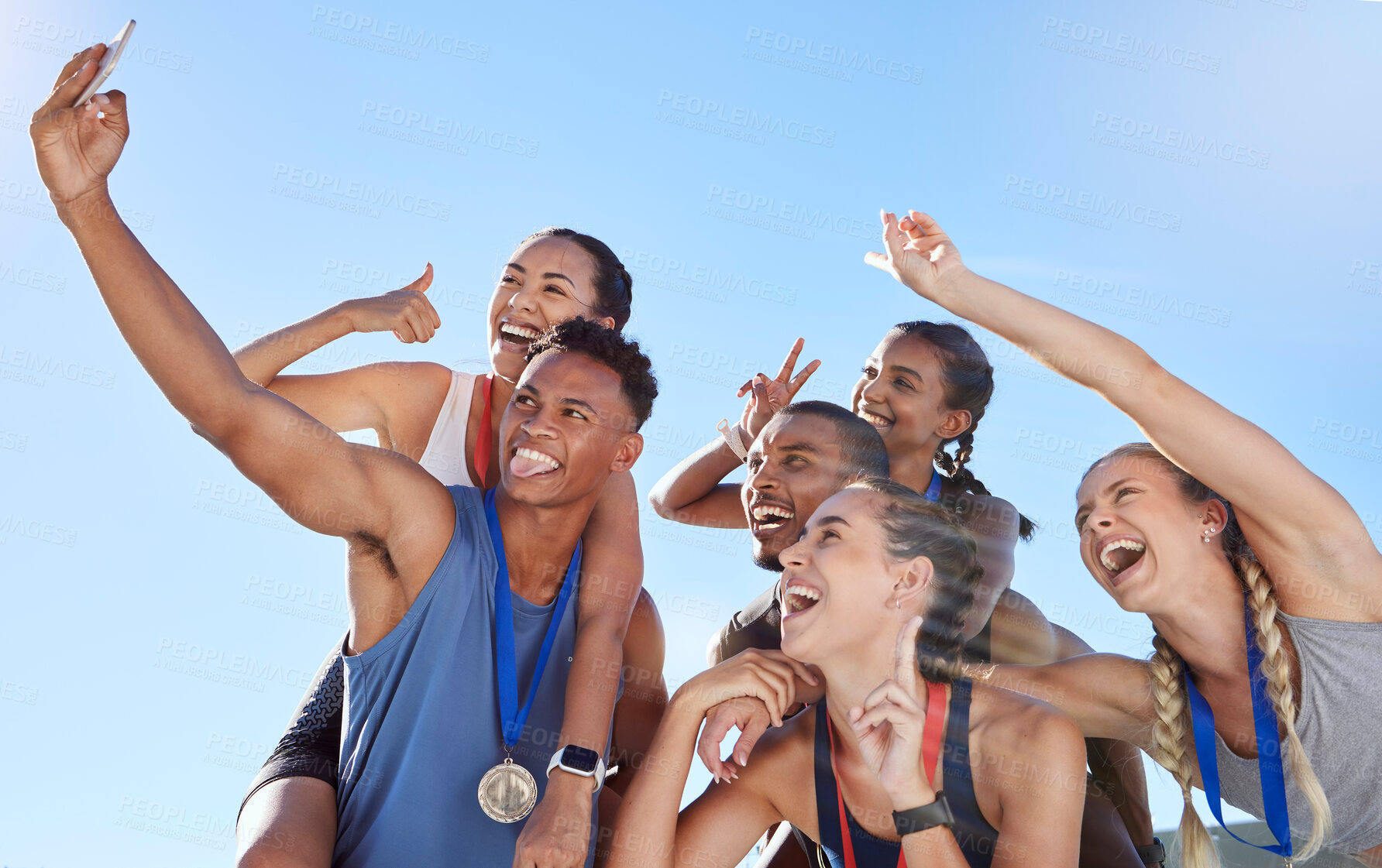 Buy stock photo Group of diverse olympic athletes taking a selfie while having fun and showing hand gestures. Happy and cheerful runners taking a photo together. Young male sprinter taking a picture with athletes