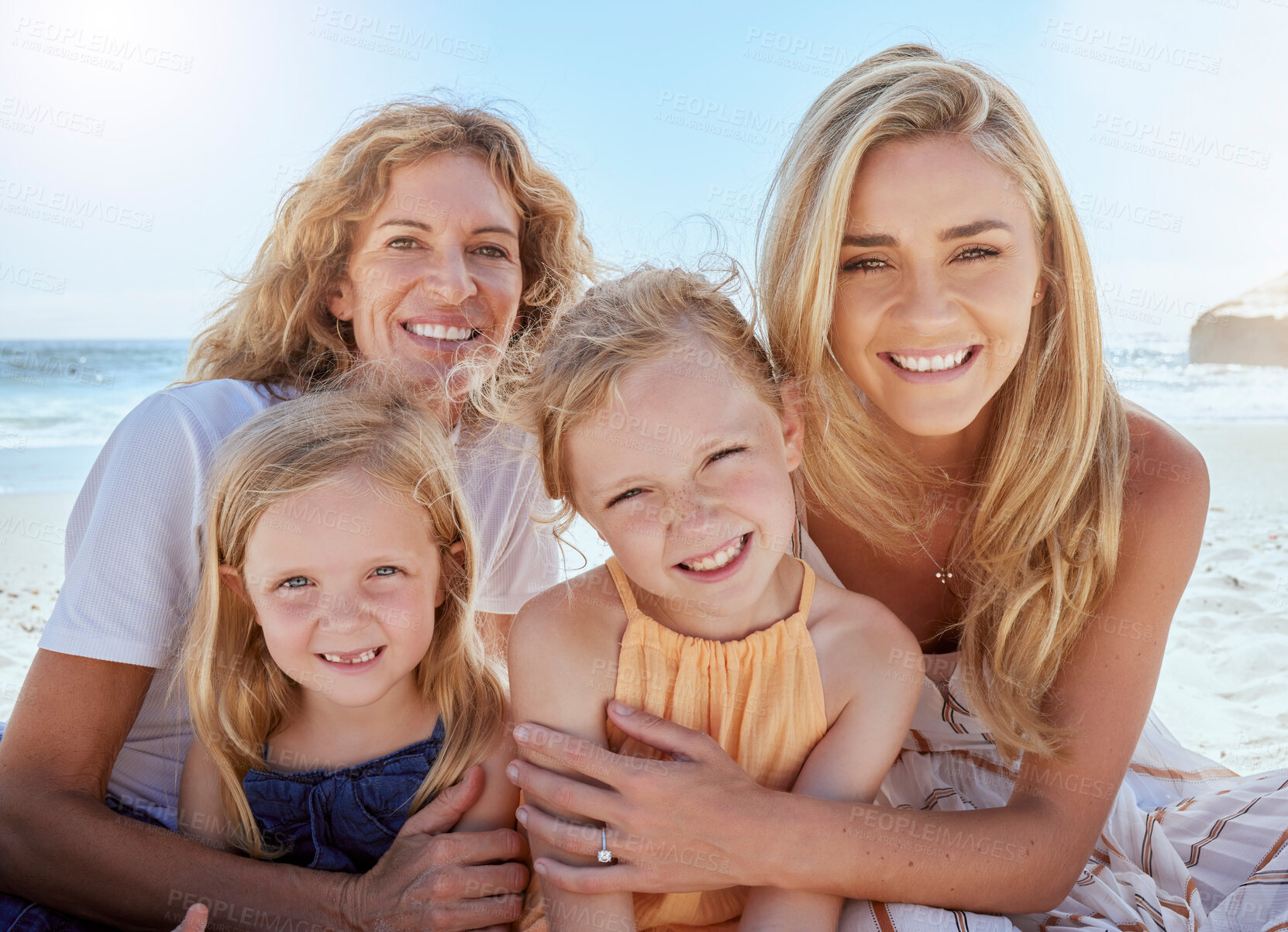 Buy stock photo Portrait of loving and caring mothers bonding and enjoying a day at beach with their little daughters. Girls sitting on the beach with their mom and grandmother while on holiday. Family at the sea